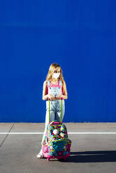 Mädchen stehend mit Schultasche gegen blaue Wand an einem sonnigen Tag - JCMF01377
