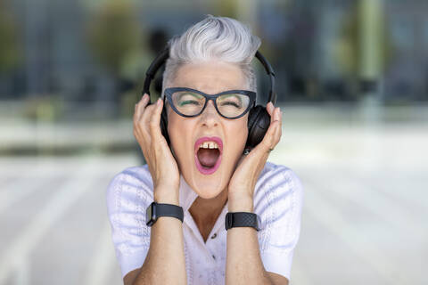 Excited senior woman screaming while listening to music through headphones stock photo