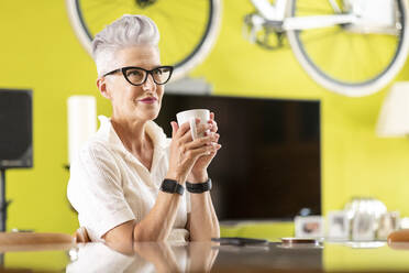 Smiling senior woman drinking coffee while sitting at home - WPEF03330