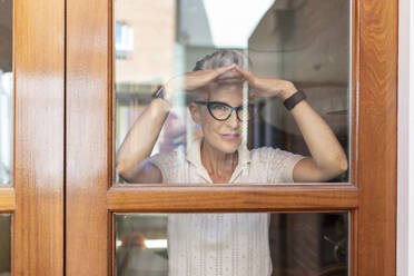 Ältere Frau macht eine Handbewegung, während sie zu Hause aus dem Fenster schaut - WPEF03338