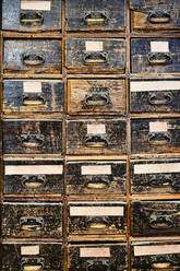 Archiv, das identische dunkelbraune Holzschubladen mit rechteckigen Griffen mit Flecken und Worten in der Werkstatt darstellt - ADSF15424