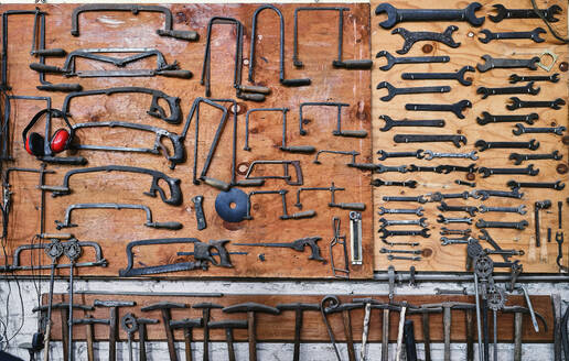 Set of different saw frames with headset near various nut wrenches above metal hammers with wooden handle on brown board in studio - ADSF15432