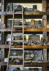 Holzregale mit verschiedenen Metalldekorationen und Leiter in einer schmuddeligen Goldschmiedewerkstatt - ADSF15438