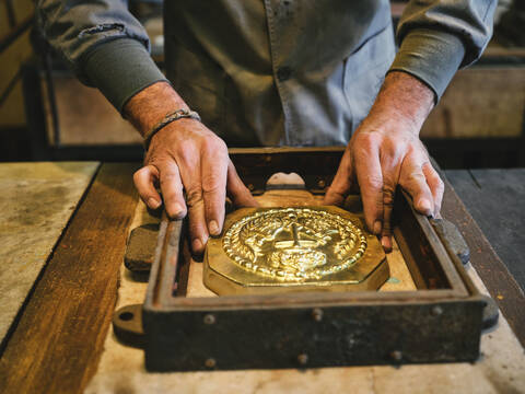 Crop unrecognizable goldsmith placing metal pattern into molding box during casting process while working in workshop stock photo