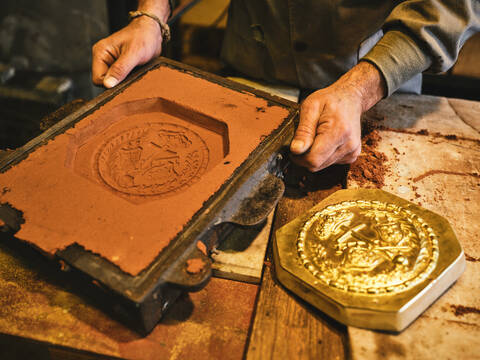 Crop unrecognizable male goldsmith showing sand in molding box while preparing mold for metal casing in workshop stock photo