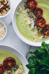 From above bowls with delicious avocado and apple cream soup decorated with sun dried tomatoes and toasted grated coconut with cashew nuts and fresh basil - ADSF15450