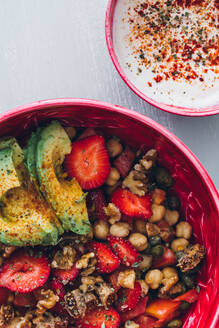 Top view Zusammensetzung der Ernte anonyme weibliche mit Schüssel leckere gesunde Kichererbsen und Avocado-Salat mit reifen Erdbeeren und Walnüssen in der Nähe von Schüssel mit Sahne-Sauce und hölzernen Besteck gekrönt - ADSF15453