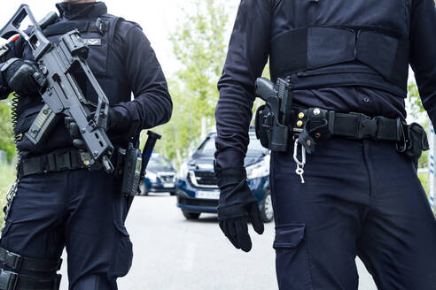 Spanische Polizeibeamte in Schutzkleidung mit Gewehren und medizinischen Masken bei einer Straßenpatrouille - ADSF15479