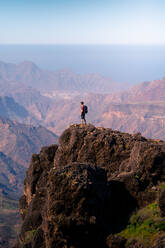 Side view of unrecognizable tourist standing on rough rock and enjoying breathtaking view of highland area in Gran Canaria - ADSF15481