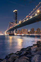 Erstaunlicher Blick auf die beleuchtete Brooklyn-Brücke und glühende Wolkenkratzer mit Lichtern, die sich im Wasser in der Nacht spiegeln New York City - ADSF15497