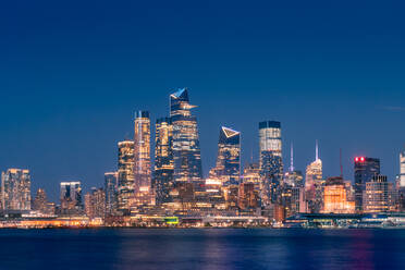 Stadtbild von New York City mit leuchtenden Wolkenkratzern und beleuchteter Uferpromenade bei Nacht - ADSF15499