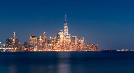 Stadtbild von New York City mit leuchtenden Wolkenkratzern und beleuchteter Uferpromenade bei Nacht - ADSF15500