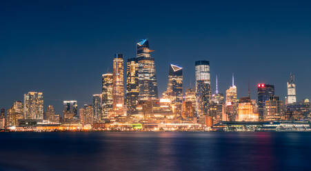 Stadtbild von New York City mit leuchtenden Wolkenkratzern und beleuchteter Uferpromenade bei Nacht - ADSF15501