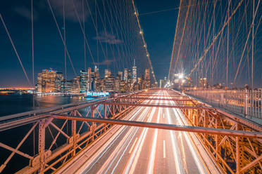 Leere Fahrbahn der beleuchteten Brooklyn-Brücke bei Nacht mit leuchtenden Wolkenkratzern im Hintergrund in New York City - ADSF15502