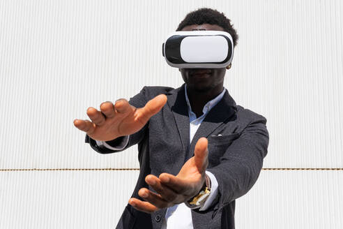 Afroamerikanischer Mann steht und erlebt virtuelle Realität, während er ein modernes VR-Headset auf gelbem Hintergrund in einer Stadt benutzt - ADSF15508