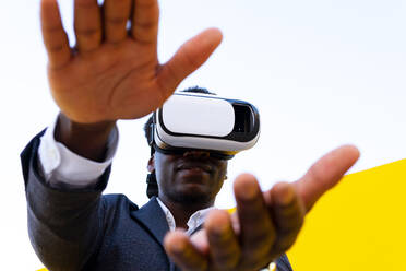African American male standing experiencing virtual reality while using modern VR headset on yellow background in city - ADSF15509