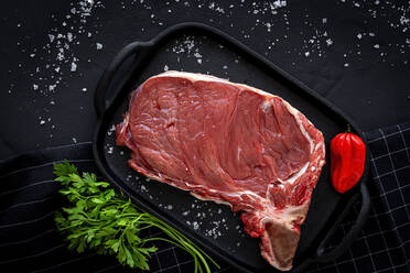 Fresh raw T-bone beef steak with red pepper, tomato, pink pepper and parsley ready to cook from above. Flat lay. Top view - ADSF15532