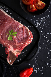 Frisches rohes T-Bone-Rindssteak mit roter Paprika, Tomate, rosa Pfeffer und Petersilie, bereit zum Garen von oben. Flachlage. Ansicht von oben - ADSF15535