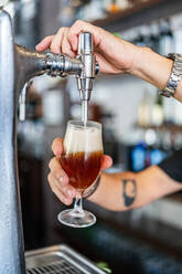 Abgeschnittene, nicht erkennbare Person, die Bier von einer Biersäule in ein Glas gießt, während sie als Barkeeper in einer modernen Bar arbeitet - ADSF15538