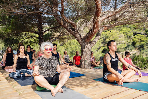 Von oben Gruppe von verschiedenen Menschen meditieren in Lotus-Pose während der Yoga-Praxis in tropischen Resort am sonnigen Tag - ADSF15549