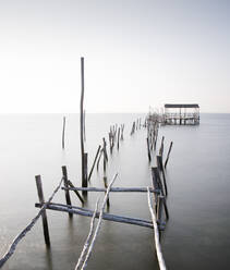 Verlassenes, teilweise zerstörtes Dock aus dicken Holzstäben am endlosen Meer mit reinem Wasser unter heiterem Himmel bei Tageslicht - ADSF15576