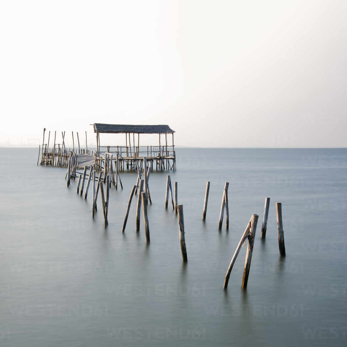 Abandoned partially destroyed dock made of thick wooden sticks on endless  ocean with pure water under serene sky in daylight stock photo