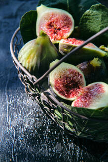 From above closeup of fresh ripe figs arranged in basket with green leaves placed on black slate board - ADSF15655