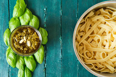 Draufsicht auf eine kleine Glasschale mit der berühmten italienischen Pesto-Sauce aus frischen Basilikumblättern und Pinienkernen, die mit Olivenöl übergossen ist, in der Nähe von köstlichen italienischen Nudeln - ADSF15661