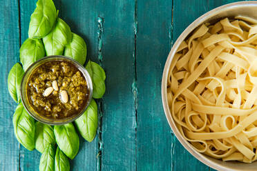 Top view of small glass bowl with famous Italian pesto sauce made of fresh basil leaves and pine nuts covered with olive oil near of delicious Italian pasta - ADSF15661