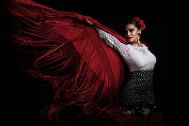 Verführerische junge Hispanierin im traditionellen roten Kostüm, die einen sinnlichen Flamenco-Tanz aufführt und wegschaut - ADSF15667