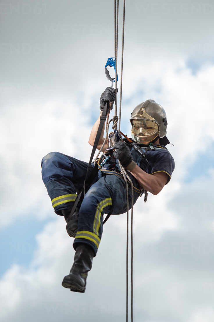 https://us.images.westend61.de/0001452838pw/side-view-of-strong-firefighter-in-protective-equipment-during-training-with-ropes-near-building-on-background-of-blue-sky-ADSF15672.jpg