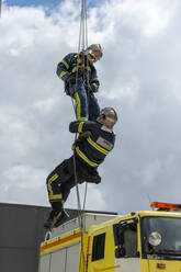 From below of firefighters in protective equipment climbing ropes near building during training - ADSF15675