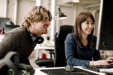 Male and female smiling professionals discussing while sitting in office - MASF19483