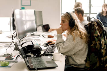 Weibliche Kollegin schaut bei der Arbeit im Büro auf den Computer - MASF19495