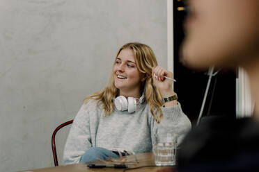 Lächelnde Geschäftsfrau mit Kopfhörern, die am Arbeitsplatz sitzt - MASF19496