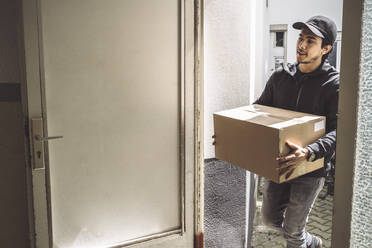 Confident delivery man with package standing at doorstep - MASF19507