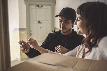 Weiblicher Kunde, der während der Paketzustellung auf dem Handy unterschreibt - MASF19509