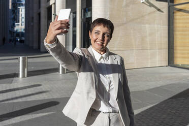 Frau nimmt Selfie, während gegen Bürogebäude stehen - VPIF02987