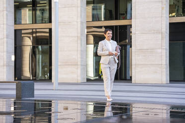 Businesswoman holding purse while standing by fountain in city - VPIF02998