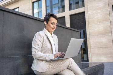 Businesswoman using laptop while sitting on bench in city - VPIF03000