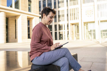 Geschäftsfrau benutzt digitales Tablet, während sie auf einer Bank in der Stadt sitzt - VPIF03019