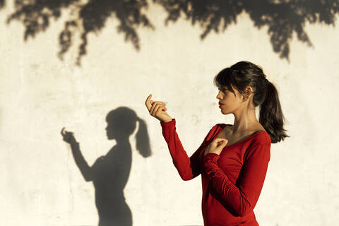 Nachdenkliche Frau, die eine Handbewegung macht, während sie im Schatten eines Baumes steht, lizenzfreies Stockfoto