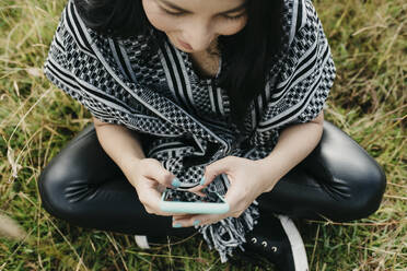 Frau schreibt Textnachrichten auf ihrem Smartphone, während sie in einem öffentlichen Park sitzt - DSIF00109