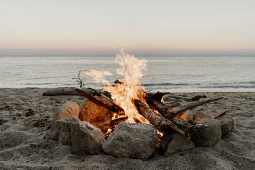 Campfire on empty beach during sunset - AFVF07231