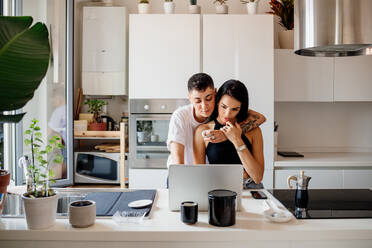 Young lesbian couple standing in kitchen, using laptop. - CUF56482