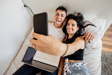 Junges lesbisches Paar liegt auf einem Bett und macht ein Selfie mit dem Handy. - CUF56486