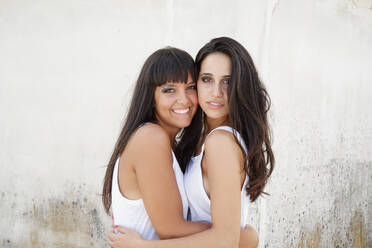 Porträt von zwei schönen jungen Frauen mit langen braunen Haaren, die sich umarmen und in die Kamera lächeln. - CUF56512