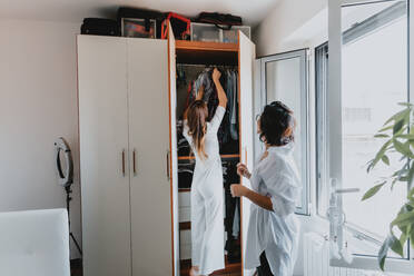 Two women with brown hair standing in an apartment, hanging clothes in wardrobe. - CUF56524