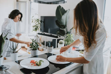 Zwei lächelnde Frauen mit braunem Haar stehen in einer Küche und bereiten Essen zu. - CUF56527