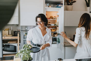 Two smiling women with brown hair standing in a kitchen, preparing food. - CUF56529